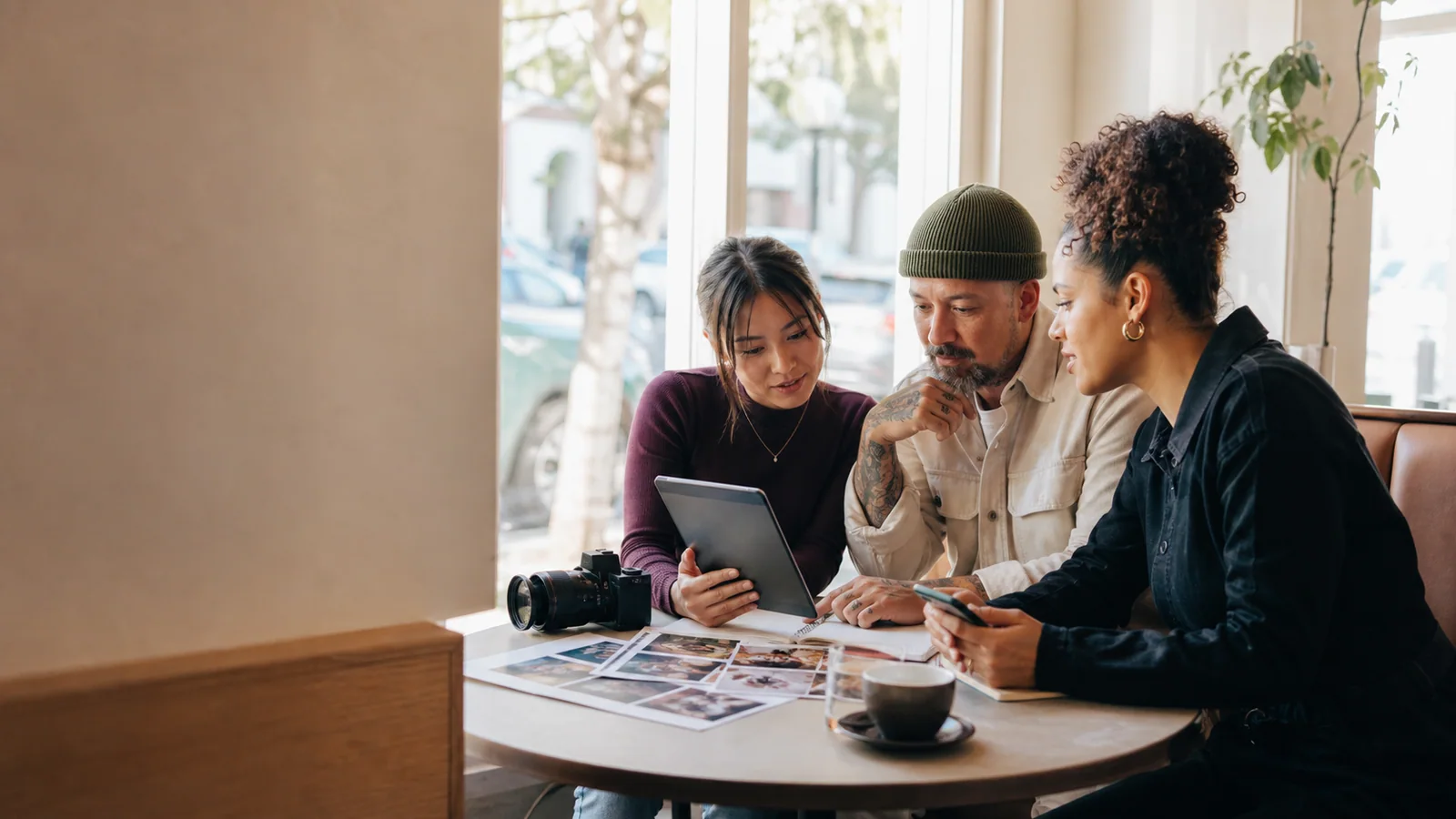 Local business owner reviewing creator portfolios with two content creators in a neighborhood cafe