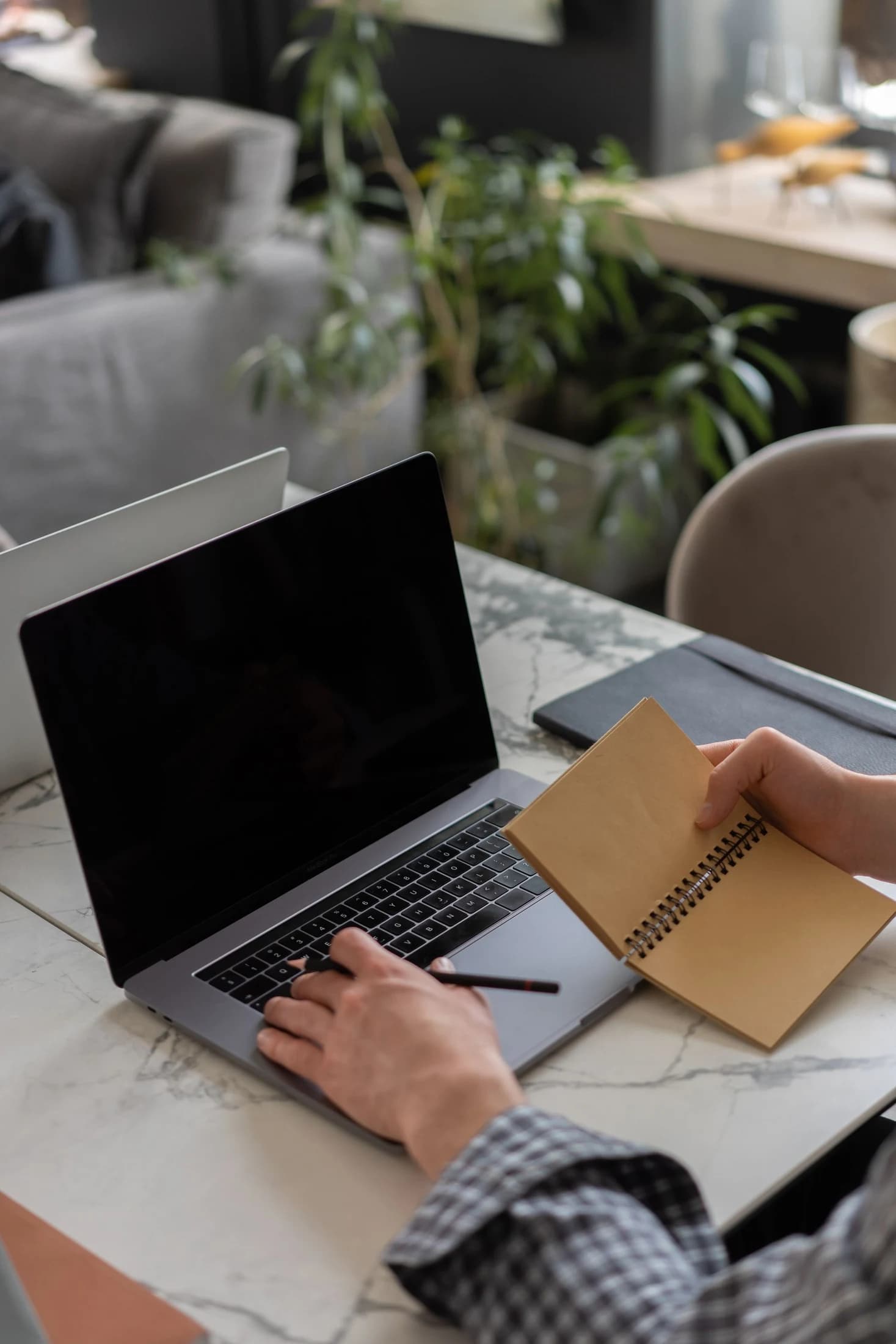 Hands writing in a notebook beside a laptop